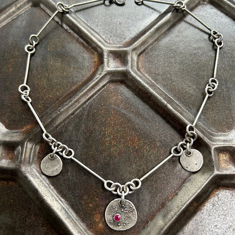 Organic “ pebbles” necklace featuring a 3.7 mm ruby on a textured surface.  $299